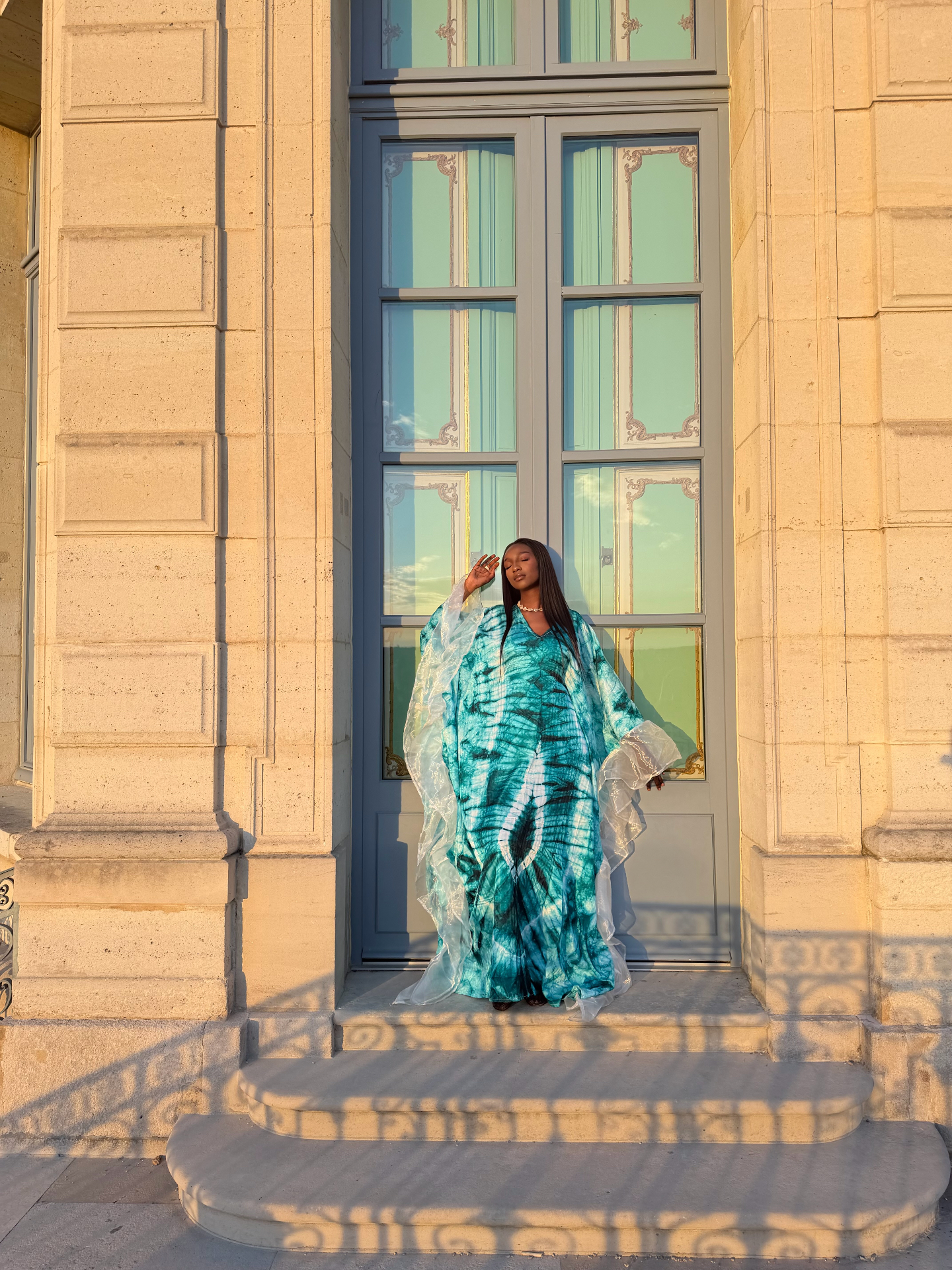 Boubou turquoise à manches en organza devant une porte haussmannienne