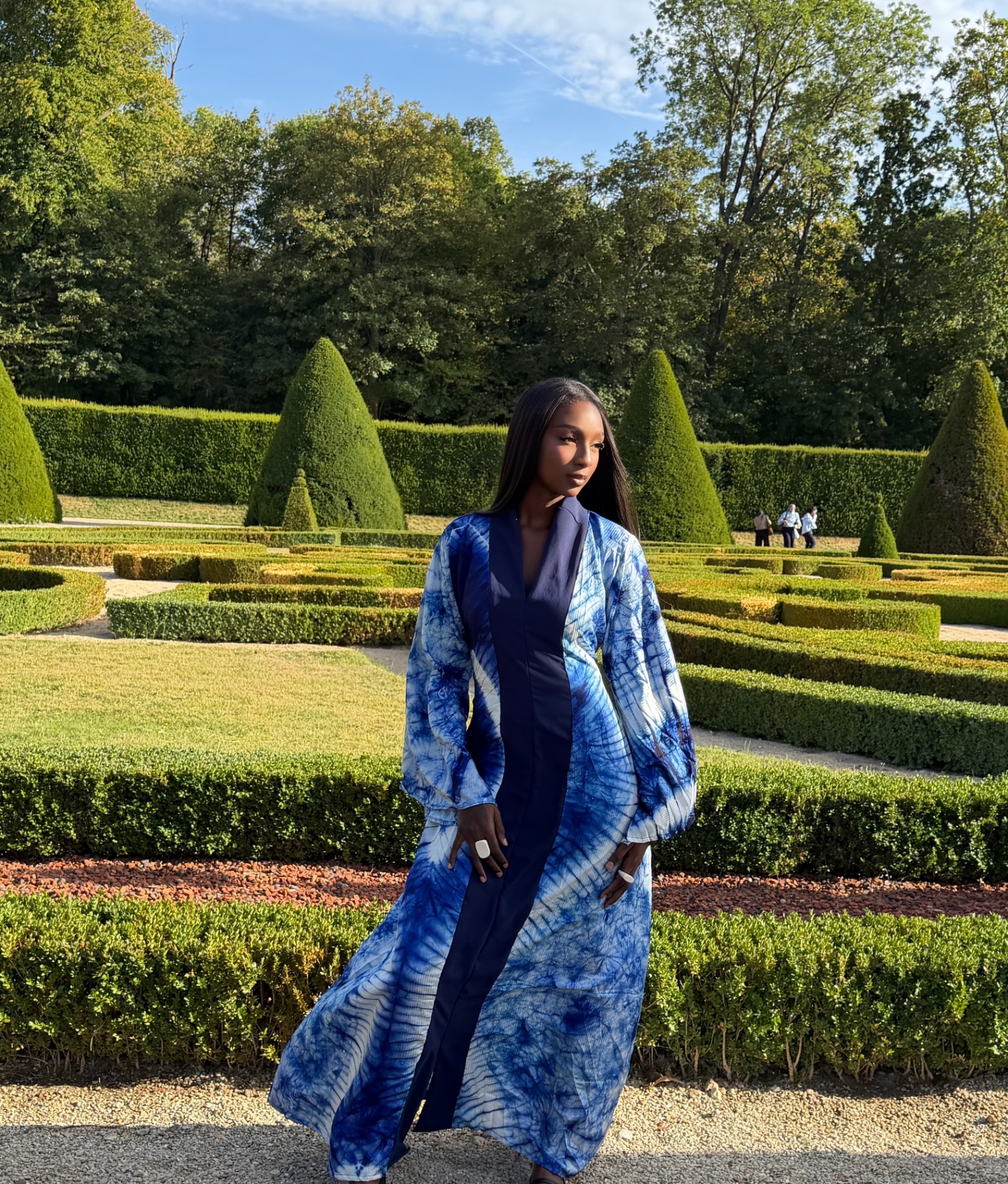 Boubou adire bleu indigo porté dans un jardin à la française